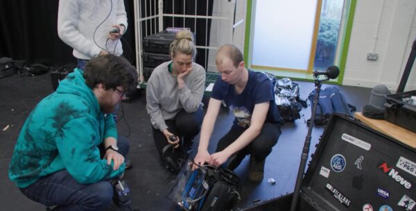 Three people crouching on the floor looking at a piece of equipment