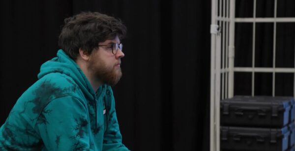 Photo of Jerome from the side, wearing glasses and a turquoise hoodie on-set